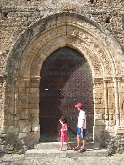 Little girl in pink dress and taller boy in white shirt and red cap looking at the portale of the Chiesa di San Francesco d'Assisi, Gerace, Calabria